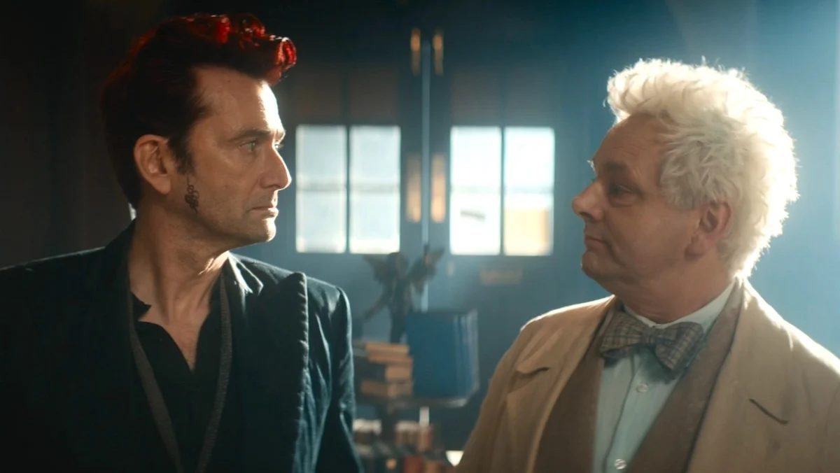 Crowley in black looks at Aziraphale in brown in the bookstore on Good Omens 3
