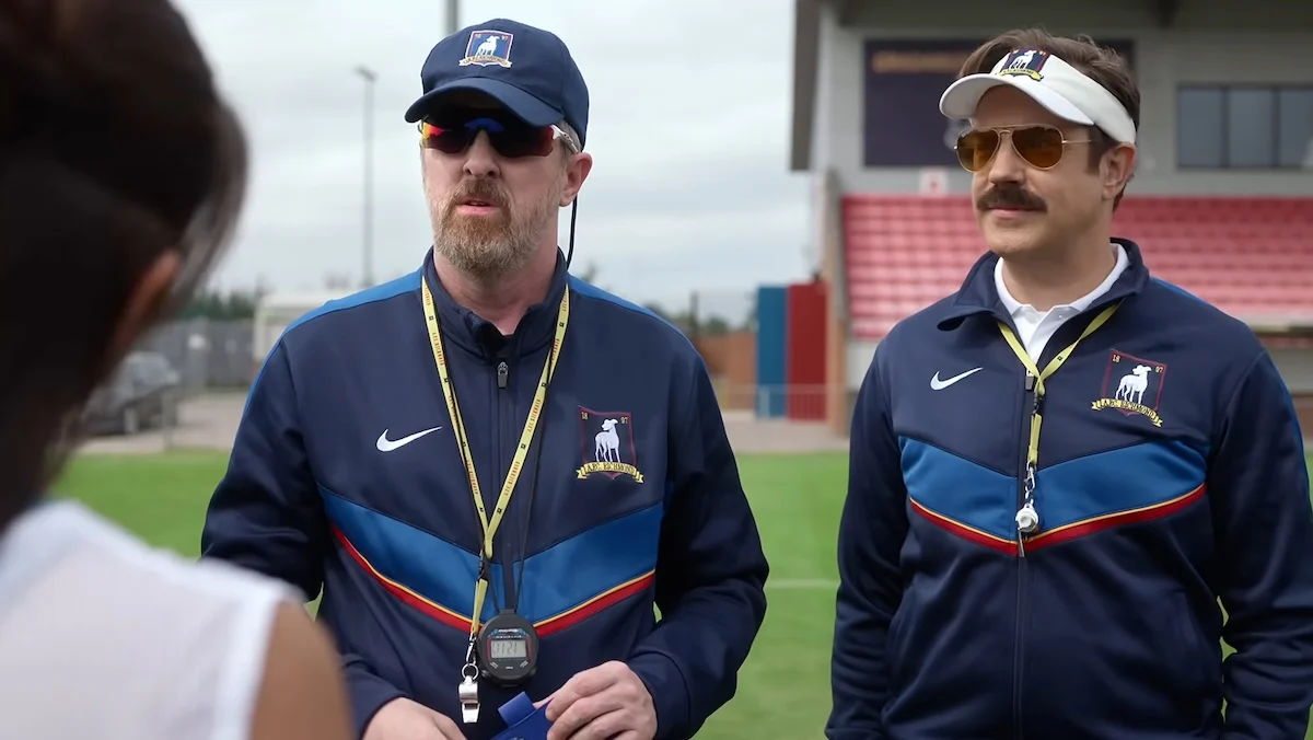 Coaches Beard and Lasso talk to a player at training in a still from ted Lasso season 4