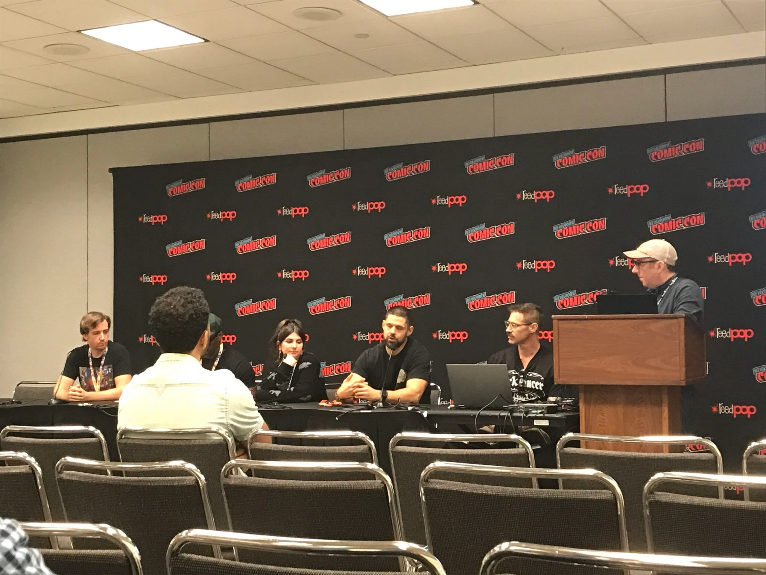 A view of the Rocketship Entertainment panel, the panelists are sitting in front of a NYCC and reedpop banner with one person visibly seated in the front row, but other nearby seats remain empty. 