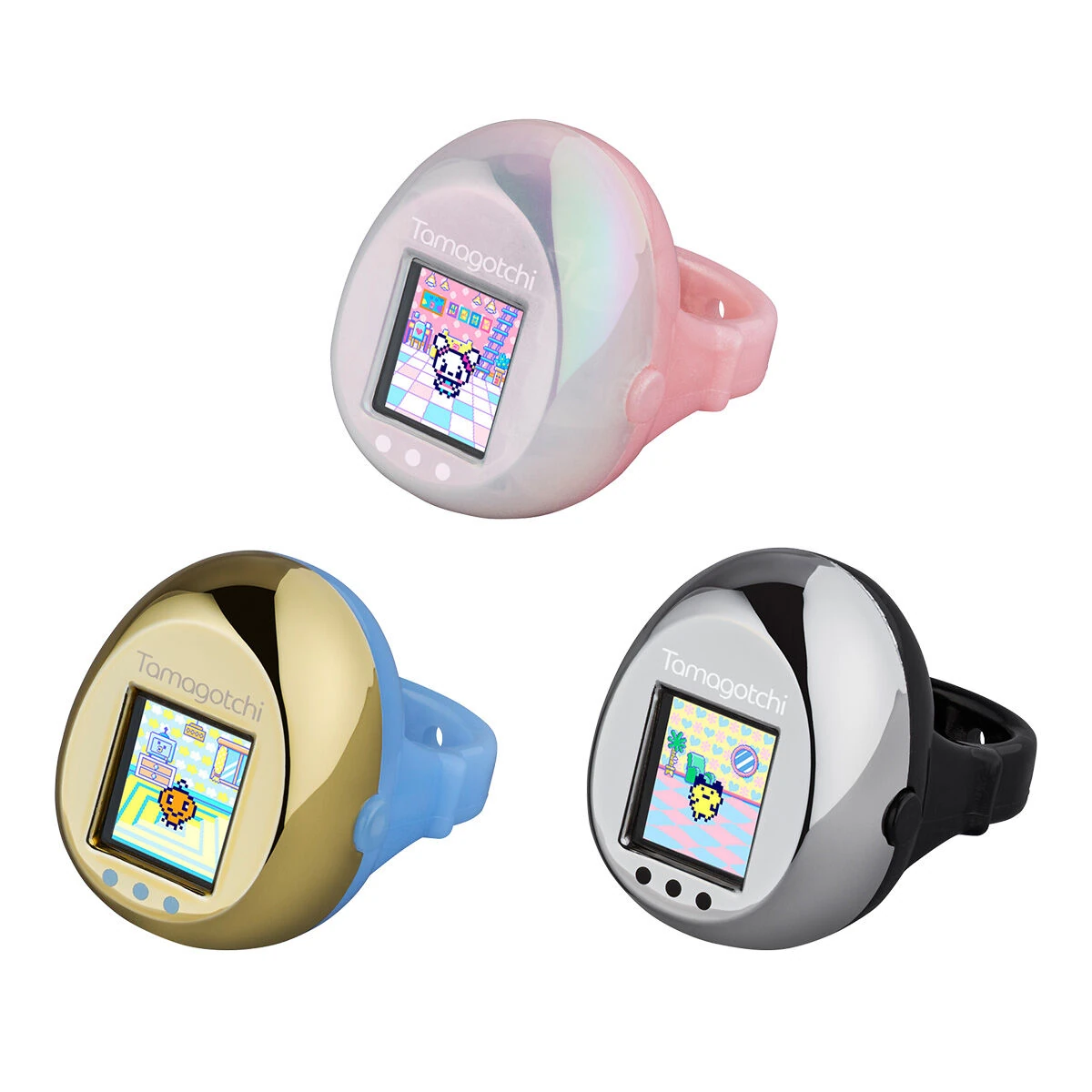 Three Tamagotchi rings against a solid white backdrop. The top ring is pink and white, bottom left is gold and light blue, bottom right is silver and black. 